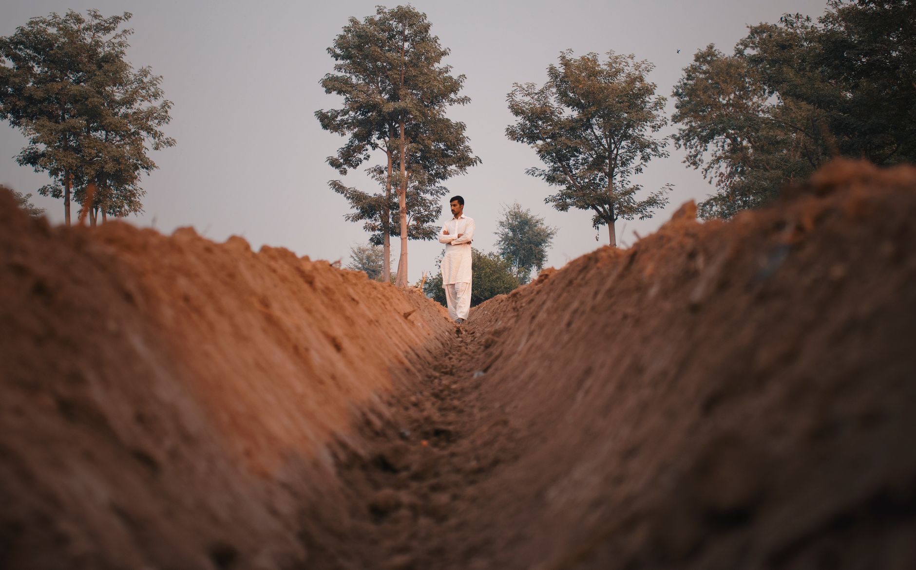 A man standing in a trench of an agricultural field surrounded by trees, conveying rural life and nature
